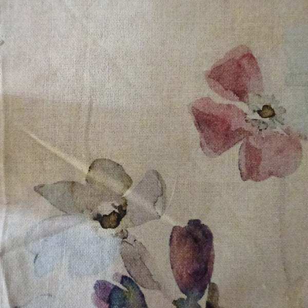 A close-up of a light beige fabric with a watercolor floral print featuring pink, purple, and gray flowers.